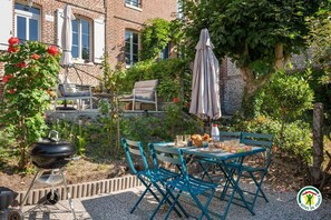Eine Terrasse mit Tisch, Stühlen, einem Grill und einem Sonnenschirm.