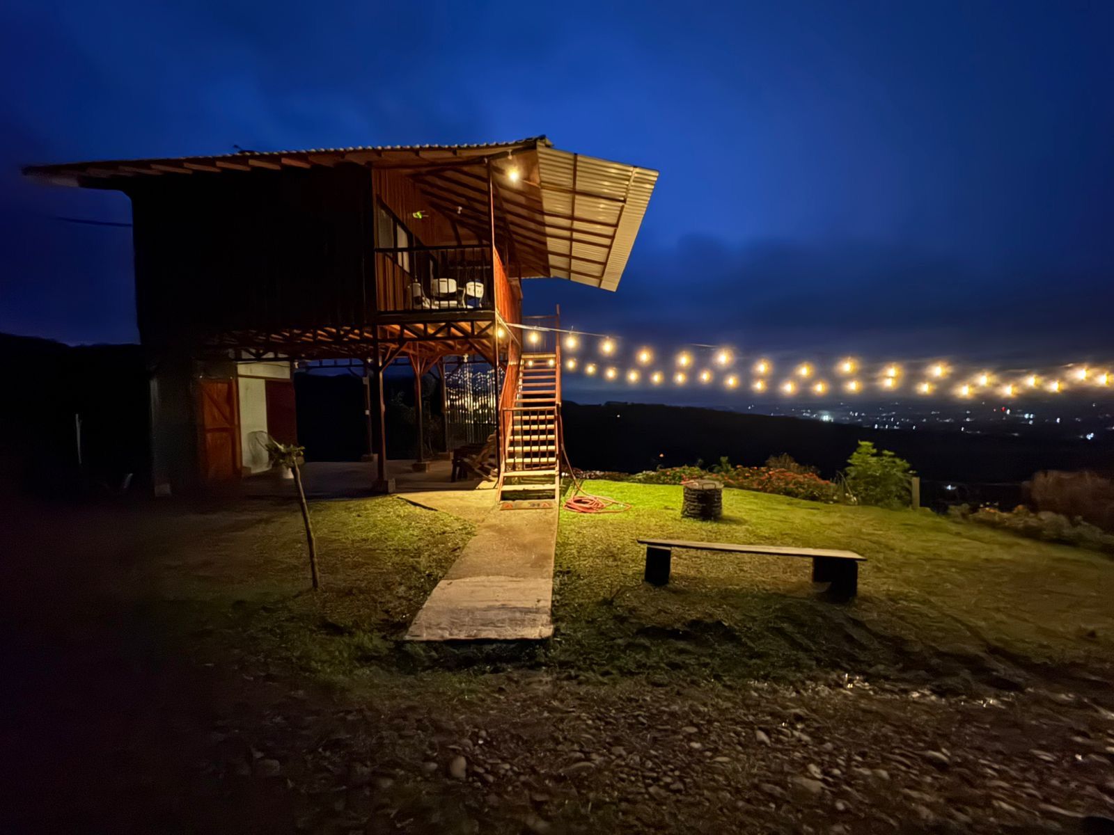 A two-story building with a wooden exterior and a balcony, surrounded by a well-maintained lawn and a string of lights.