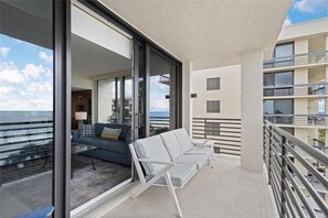 Ein Balkon mit einer Couch und Stühlen, eine Glastür zu einem Wohnbereich und Blick aufs Meer.