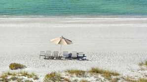 Une plage avec une rangée de transats sous un grand parasol, une plage de sable et une mer calme.