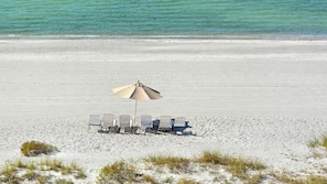 Ein Strand mit einer Reihe von Liegestühlen unter einem großen Sonnenschirm, feinem Sand und ruhigem Meer.
