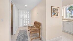 Un couloir avec un banc en bois, un tapis à motifs, une porte blanche et un tableau encadré accroché au mur.