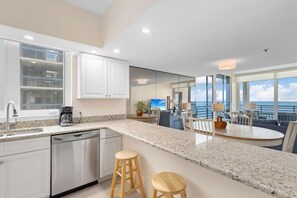 A modern kitchen with granite countertops, white cabinetry, a dishwasher, and a dining area with a view of the ocean. - Stunning Beachfront 2 BR Condo (Longboat Key)