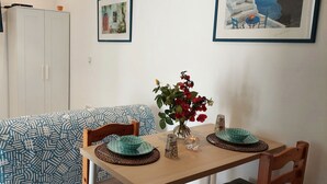 Un coin repas avec une table dressée pour deux personnes, un canapé à motifs, un vase rempli de fleurs et des œuvres d’art encadrées accrochées au mur.