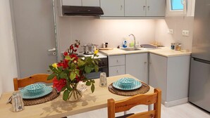 Une cuisine moderne avec des meubles gris, un réfrigérateur en acier inoxydable et une table à manger dressée avec des assiettes et un vase de fleurs.