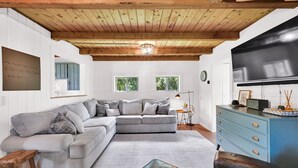 Uma sala de estar aconchegante com um sofá seccional cinza, um aparador azul e teto de madeira.