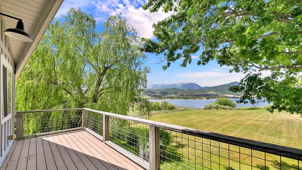 Um deck de madeira com guarda-corpo de metal, com vista para um lago e montanhas.