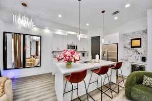 A modern kitchen with white cabinets, a central island with stools, a chandelier, and a marble backsplash. - Quiet Elegance• 2 Homes •NRG Stadium • Med Center • Sleeps 20+ Large Group Stays (Houston)