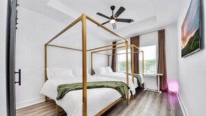 Ein modernes Schlafzimmer mit einem Himmelbett, einem Deckenventilator und einem großen Fenster mit Vorhängen.
