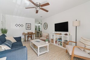 Ein modernes Wohnzimmer mit Deckenventilator, Flachbildfernseher, Bücherregal und Essbereich mit Tisch und Stühlen.