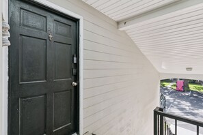 A black door with a keypad lock, a white exterior wall, and a covered porch area. - The Elliott, Ocean Walk Getaway, Pools & Walkable Location (St. Simons Island)