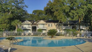 A pool area with lounge chairs, a palm tree, and a building with balconies. - The Elliott, Ocean Walk Getaway, Pools & Walkable Location (St. Simons Island)