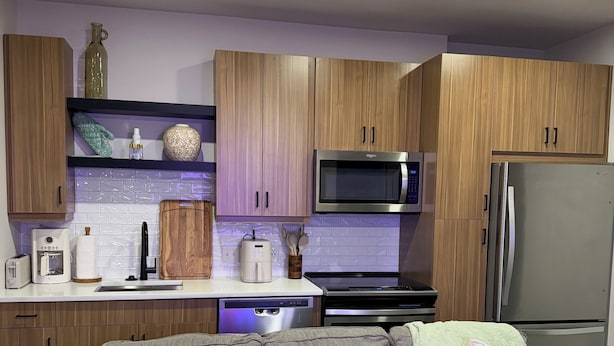 Una cocina moderna con armarios de madera, un microondas, un refrigerador y un sofá gris con cojines.