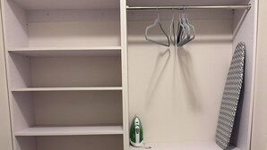 Un armario de acceso directo con varios estantes, una barra para colgar ropa y una tabla de planchar plegada.