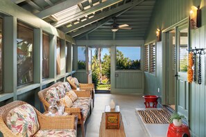 A covered porch with wicker furniture, a ceiling fan, and a view of palm trees. - 2BR West Maui condo with pool, patio, AC, and full kitchen -ICC 4 (Lahaina)
