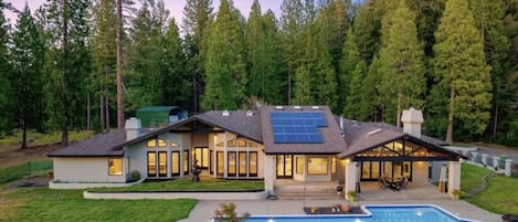 A modern house with a swimming pool, solar panels, and a forested backdrop.