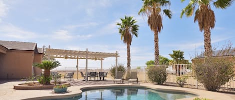 Un espace piscine agrémenté d’une pergola, de palmiers et de mobilier d’extérieur.