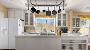 A modern kitchen with white cabinetry, a central island, hanging pots, and a window with a view. - Vineyard Estate & Water Tower | Hot Tub | Views (Sebastopol)