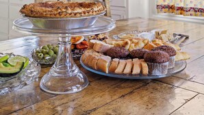 A dining table with a variety of baked goods and a cake, a chandelier, and a kitchen with cabinets and a window. - Vineyard Estate & Water Tower | Hot Tub | Views (Sebastopol)