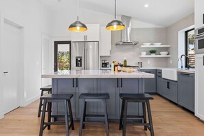 Una cucina moderna con isola centrale, sgabelli da bar, illuminazione a sospensione ed elettrodomestici integrati.