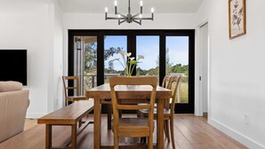 A dining area with a wooden table and chairs, a bench, a chandelier, and a view through large glass doors. - Sonoma Retreat w/ Deck, Views & BBQ (Sonoma)