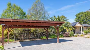 Un espacio al aire libre techado con suelo de grava, rodeado por una cerca de madera y varios árboles.