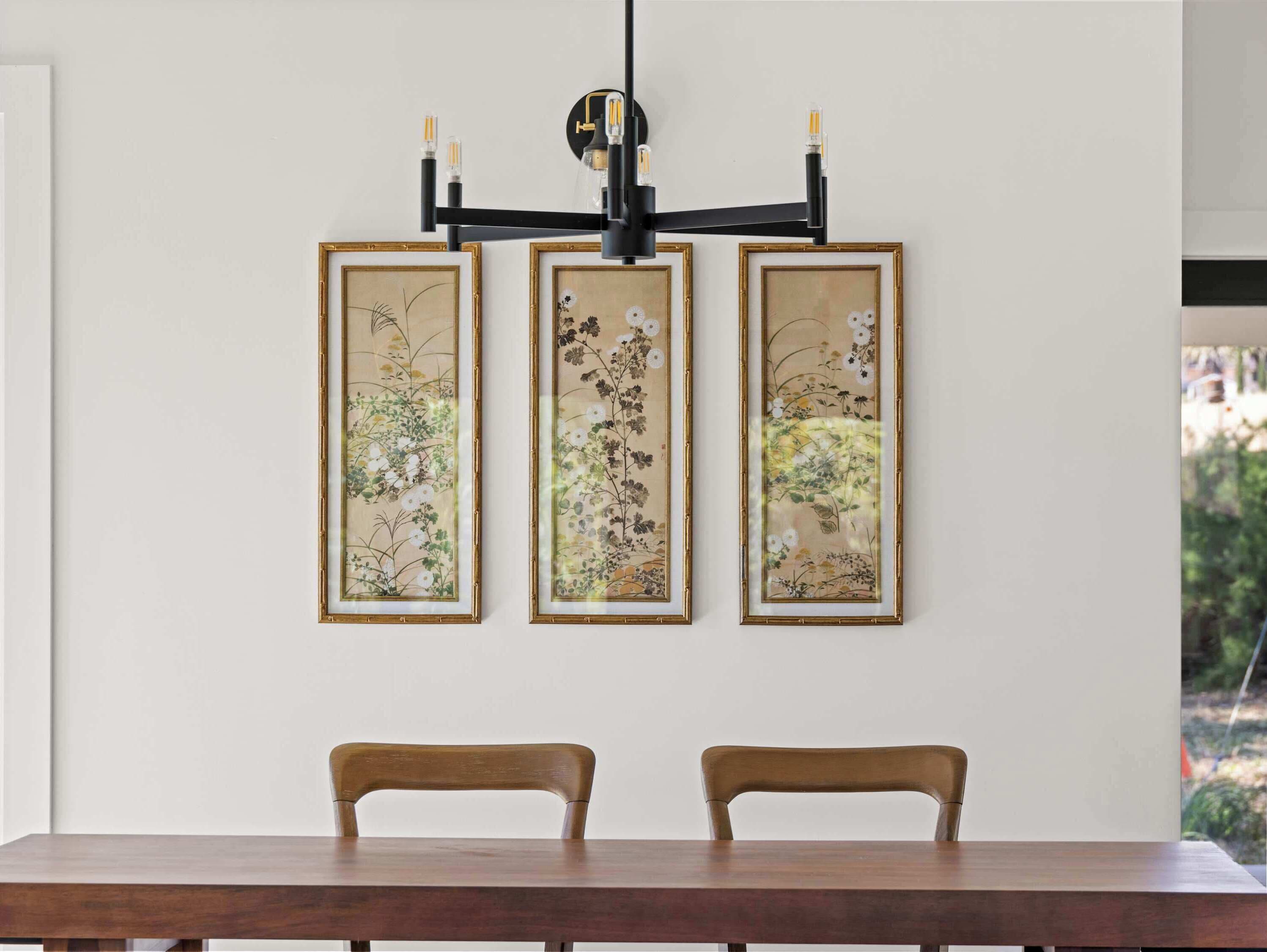 A dining area with a table and two chairs, a wall-mounted light fixture, and three framed botanical prints.