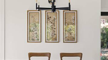 A dining area with a table and two chairs, a wall-mounted light fixture, and three framed botanical prints.