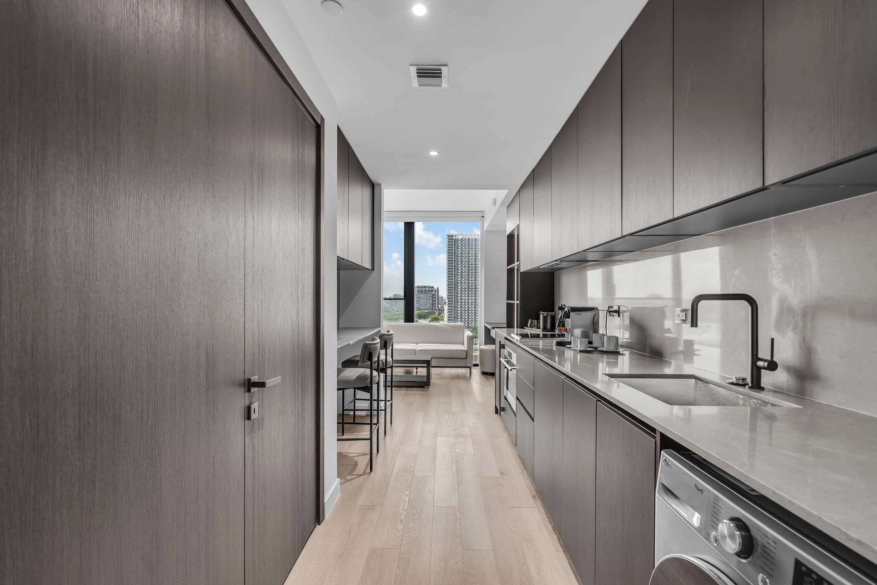 A modern kitchen with stainless steel appliances, a dining area with a sofa and chairs, and a view of the cityscape.