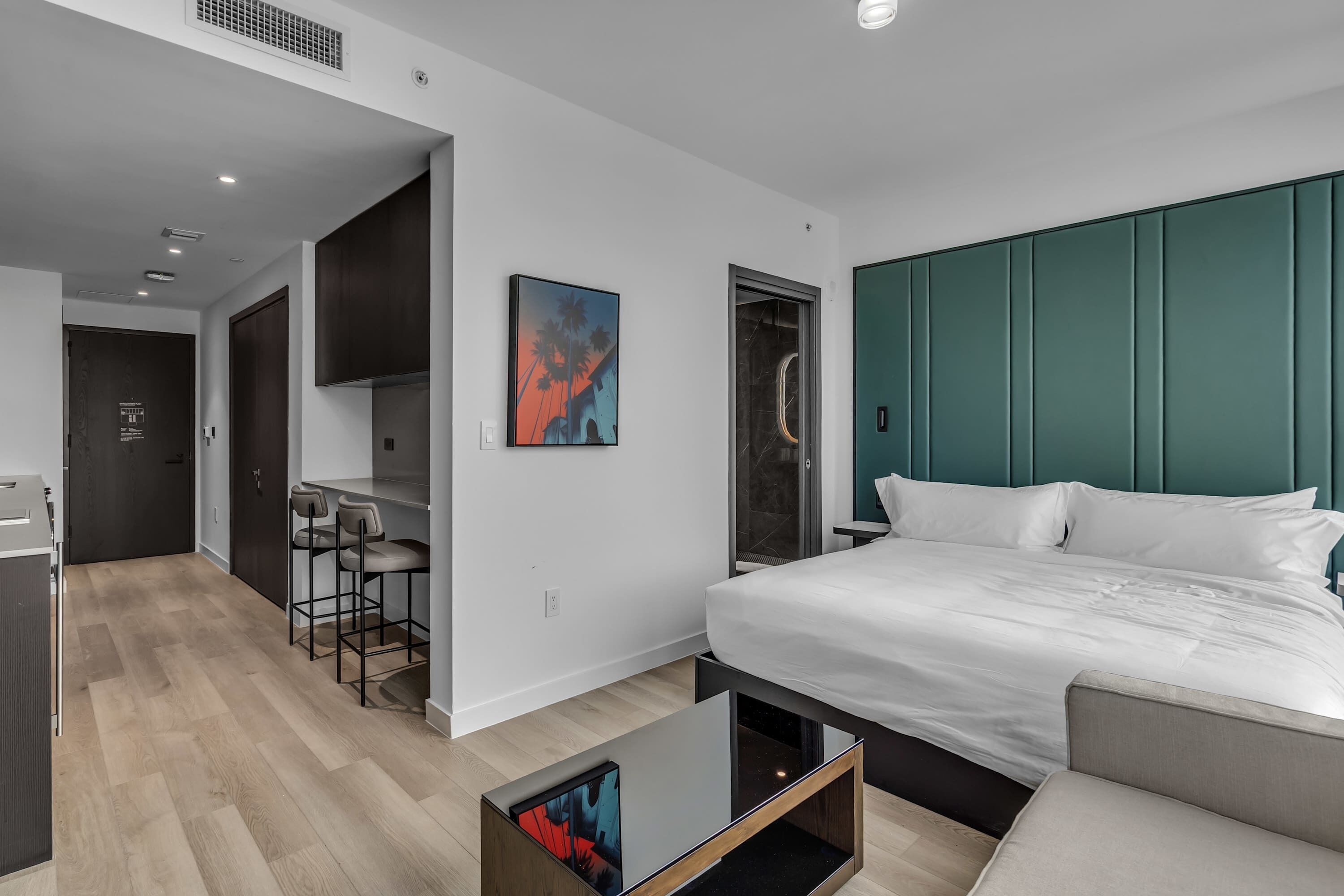 Quarto de hotel moderno com uma cama, uma escrivaninha e uma cozinha compacta.