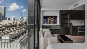 Quarto de hotel moderno com vista para a cidade, uma janela grande, um sofá, uma cozinha e uma televisão de tela plana.