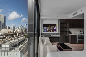 A modern hotel room with a city view, a large window, a sofa, a kitchen area, and a flat-screen TV. - Magic City & Rooftop Pool (Miami)