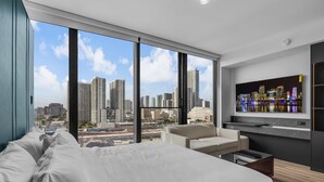 Quarto de hotel moderno com uma cama grande, um sofá, uma TV e vista para a cidade.
