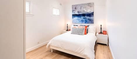 A bedroom with a bed, nightstands, a ceiling fan, a window, and a wall-mounted artwork.