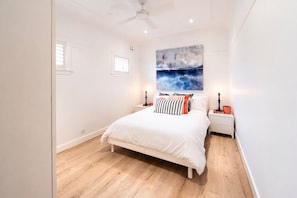 Ein Schlafzimmer mit einem Bett, Nachttischen, einem Deckenventilator, einem Fenster und einem an der Wand befestigten Kunstwerk.