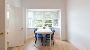 A room with a white table and blue chairs, a white door, and a window with blinds. - BONDI HAVEN- CHIC 2 BEDROOM APARTMENT (Bondi)