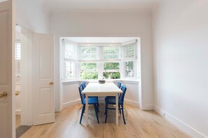 Ein Zimmer mit einem weißen Tisch, blauen Stühlen, einer weißen Tür und einem Fenster mit Jalousien.