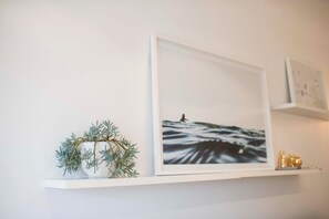 Ein weißes Regal mit einem gerahmten Bild von Meerlandschaft, einer kleinen Pflanze und einigen dekorativen Flaschen.