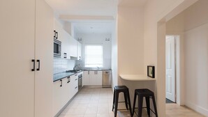 A modern kitchen with white cabinets, a microwave, stove, and a dishwasher. There are two black stools and a small white counter. - BONDI HAVEN- CHIC 2 BEDROOM APARTMENT (Bondi)