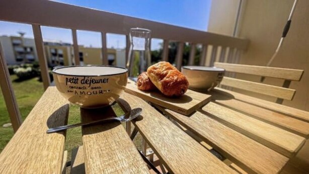 Una mesa de madera con un tazón de yogur, un croissant y un cuchillo.