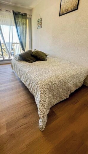 A bedroom with a bed, a window with curtains, and a framed picture on the wall. - Studio for 4 people, air conditioning, beach 350 meters away, private balcony, aquarium just a few steps away. (Le Grau-du-Roi)