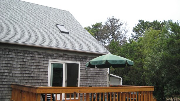 A wooden deck with a green umbrella, a barbecue grill, and a house with a gray shingled roof. - Katama Saltbox: Close to Town and Beach (Edgartown)