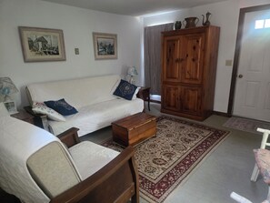 Ein Wohnzimmer mit einer Couch, einem Holzschrank und zwei gerahmten Bildern an der Wand.