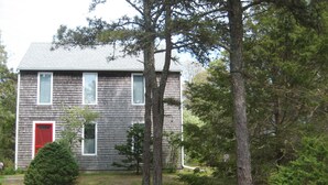 A two-story house with a red door, a small front yard, and a gravel driveway. - Katama Saltbox: Close to Town and Beach (Edgartown)