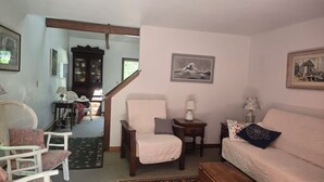 A living room with a sofa, armchairs, a wooden cabinet, and a staircase. - Katama Saltbox: Close to Town and Beach (Edgartown)