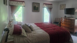 A bedroom with a bed, a dresser, a television, and two windows with curtains. - Katama Saltbox: Close to Town and Beach (Edgartown)