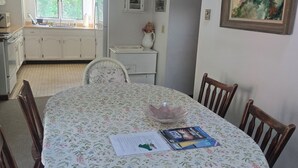 A dining area with a round table covered in a floral tablecloth, surrounded by wooden chairs. - Katama Saltbox: Close to Town and Beach (Edgartown)