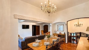 A dining area with a wooden table set for four, a chandelier, and a sofa in the background. - The House of Observance (DRAGUIGNAN)