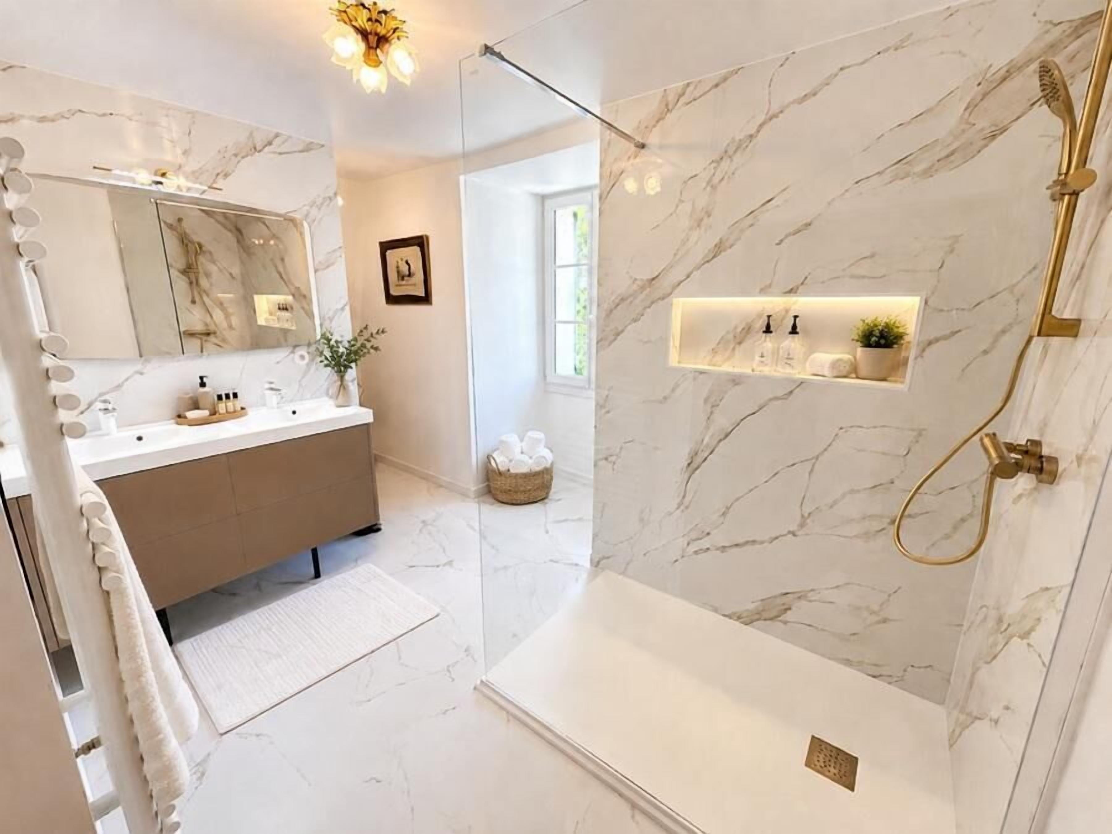 A modern bathroom with a marble vanity, a large mirror, and a walk-in shower.