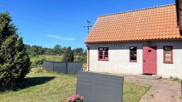 A single-story house with a red-tiled roof and a red door, surrounded by a grassy area and a metal fence.